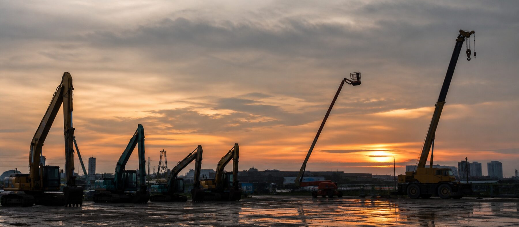 Equipment yard at dusk with parked machines silhouetted against the sky